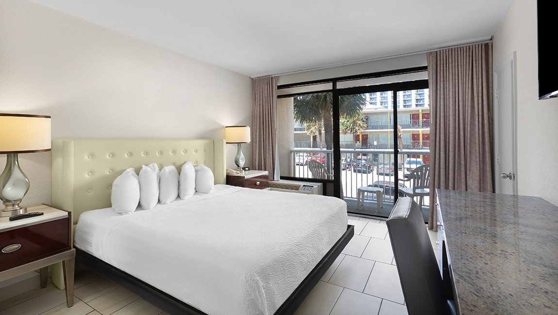 A wide hotel room with a large bed, granite countertop, and sliding glass door leading to a balcony.