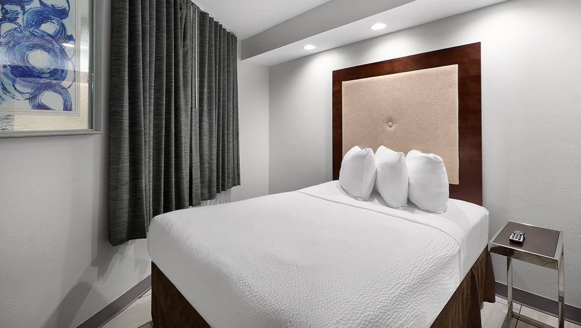 A hotel room with a large bed, nightstand, and artwork on the wall.