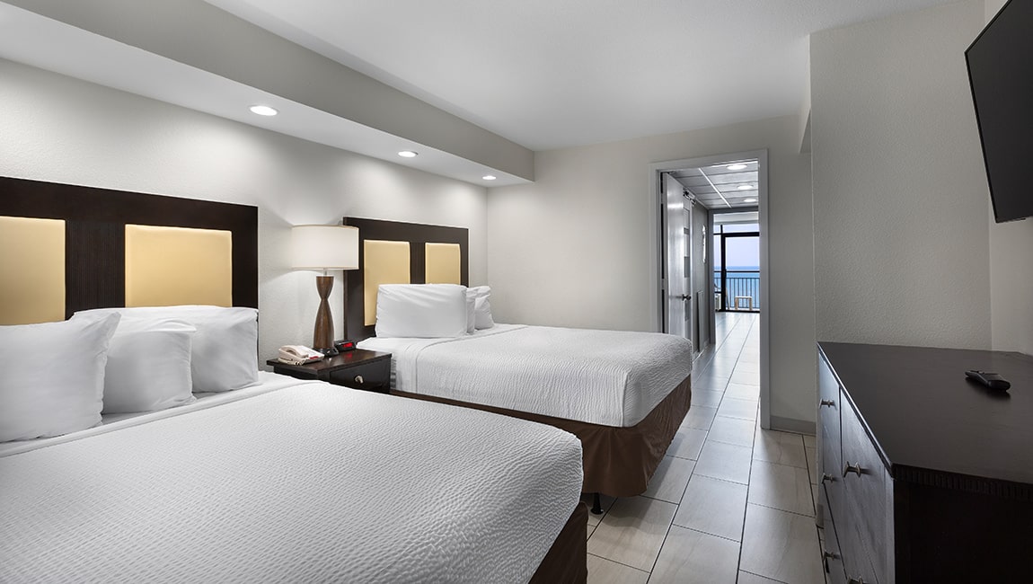 A hotel room with two double beds, a tiled floor, and a balcony door.