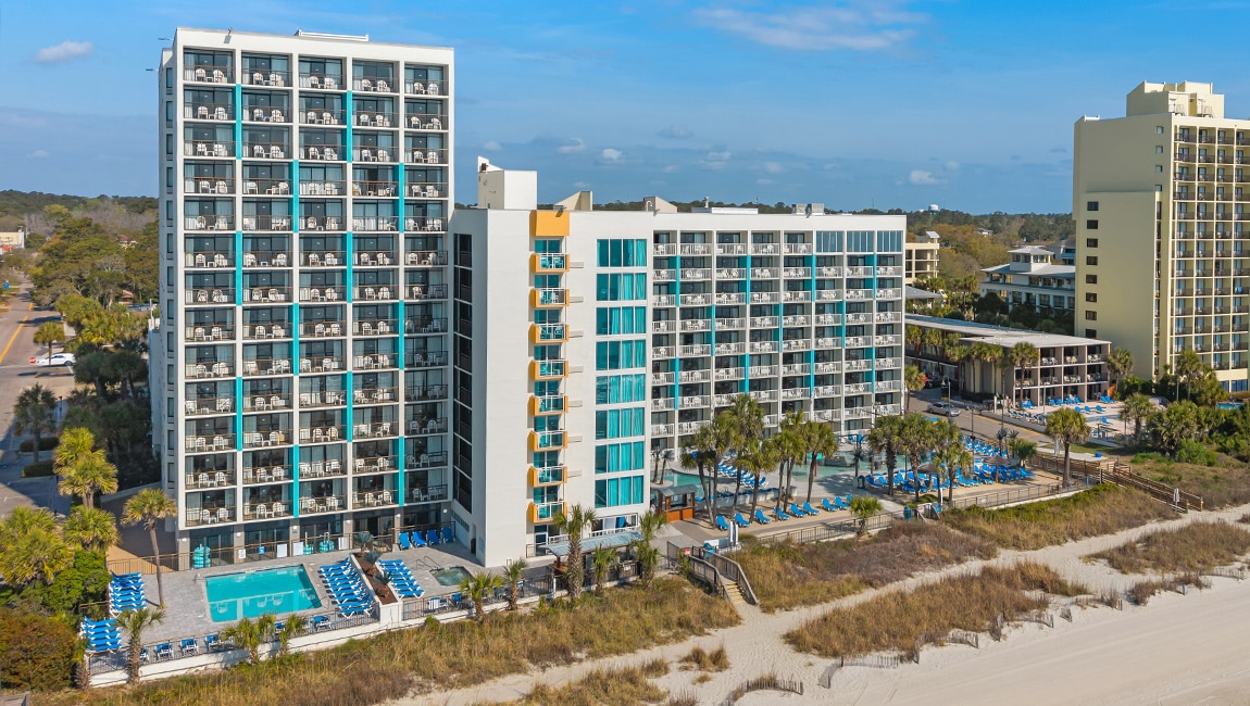 An aerial view of a large hotel with a pool and beach in front of it.