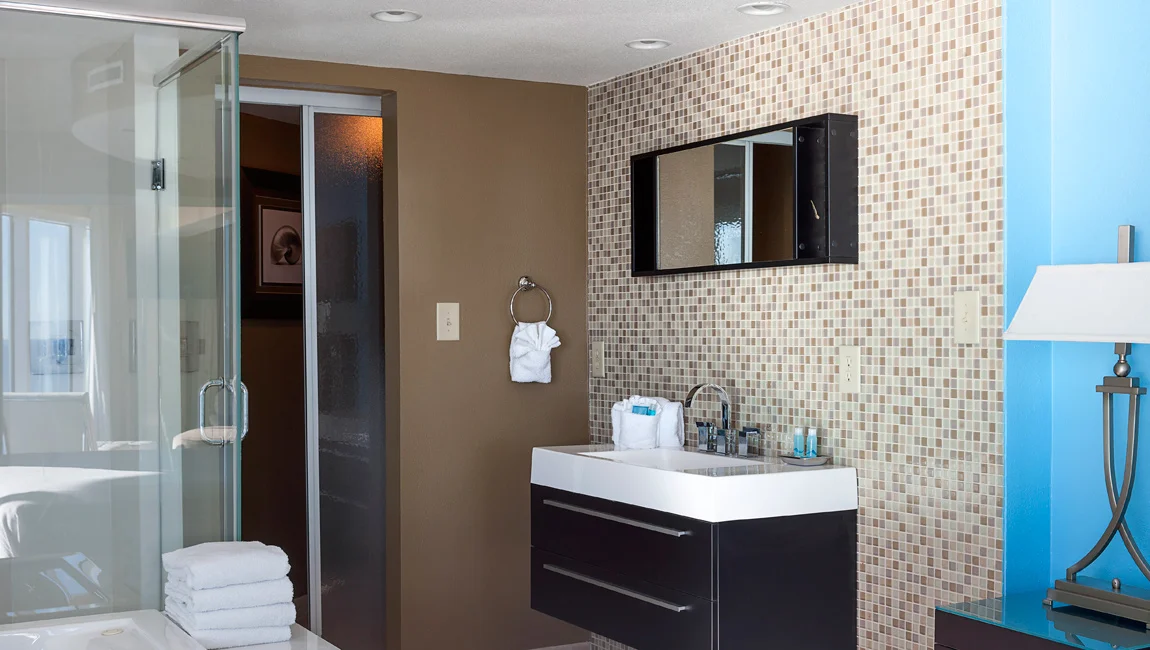 A modern bathroom with a glass shower, a white sink, and a stack of towels.