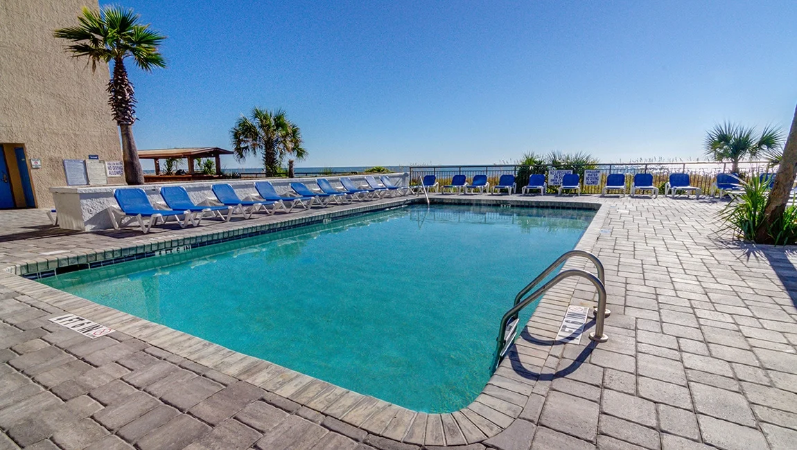A swimming pool with blue lounge chairs and palm trees, overlooking the ocean.